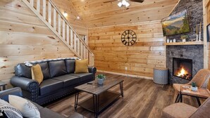A cozy cabin interior with a staircase, a fireplace, a leather sofa, and a coffee table.