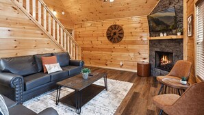 A cozy living room with a fireplace, a wooden staircase, and a leather sofa. - Amazing Grace - Newly Built - 3 BR - Less Than 2 Miles from The Island (Pigeon Forge)