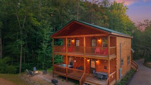 Une cabane en rondins à deux étages, dotée d’un balcon, d’un espace salon extérieur et d’un foyer.
