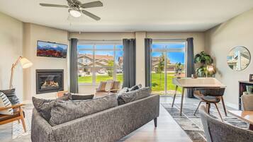 Uma sala de estar moderna com lareira, sofá, mesa de jantar e amplas janelas com vista para o bairro.
