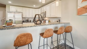 A modern kitchen with white cabinets, a granite countertop, and bar stools. - Mid-Brambleberry (Colorado Springs)
