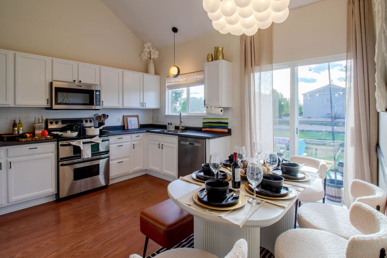 Una cocina moderna con armarios blancos, electrodomésticos de acero inoxidable y un comedor con una mesa preparada para dos.