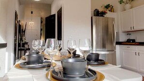 A modern dining area with a white table set for a meal, a chandelier, and a kitchen in the background. - Colorful Colorado house by DIA Airport Rockies & Downtown! (Commerce City)