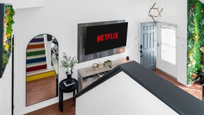 A modern living room with a flat-screen TV displaying 'NETFLIX', a colorful staircase, a small side table with a vase, and a green vertical garden wall. - Colorful Colorado house by DIA Airport Rockies & Downtown! (Commerce City)