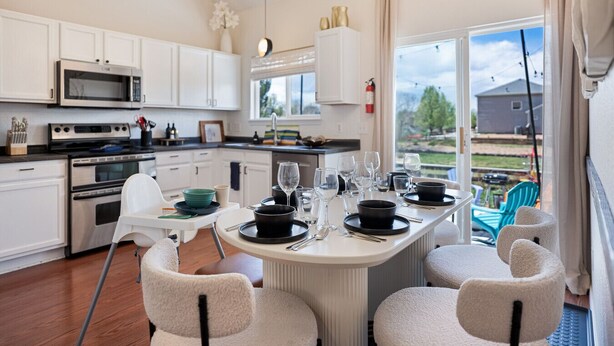 A modern kitchen with white cabinets, stainless steel appliances, and a dining area with a round table set for six. - Colorful Colorado house by DIA Airport Rockies & Downtown! (Commerce City)