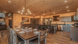 A spacious kitchen with wooden floors, a dining area with a large table set for six, and a bar area with stools. - Mountain Dreams - Mountain views for miles! (Sevierville)