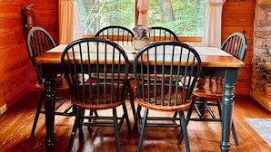 A wooden cabin interior with a dining table, four chairs, a chandelier, and a fireplace.