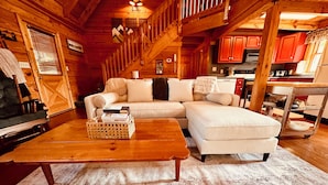 A cozy log cabin interior with a living room featuring a sectional sofa, a wooden coffee table, and a fireplace.