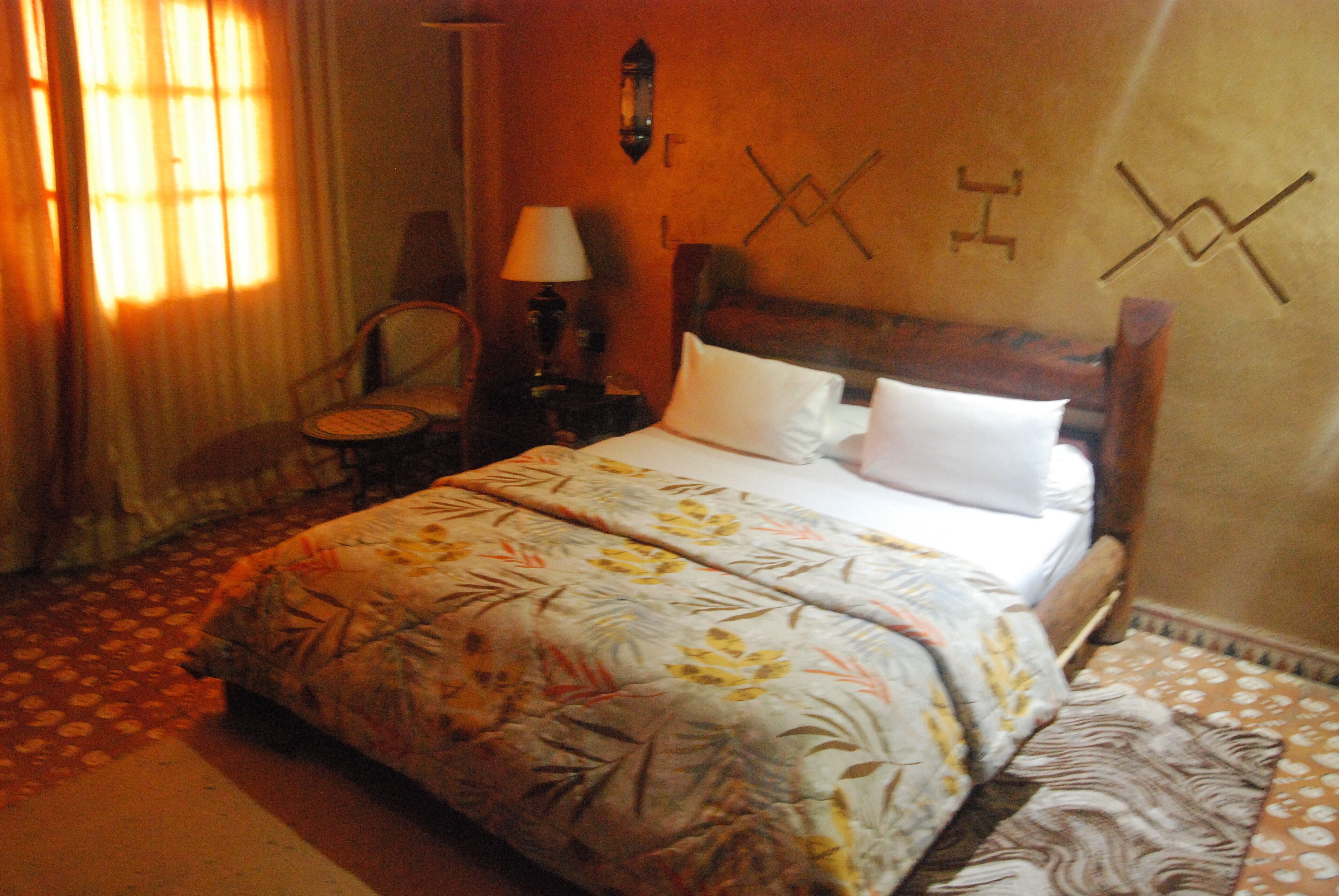 A hotel room with a bed, a chair, a nightstand, and a lamp.