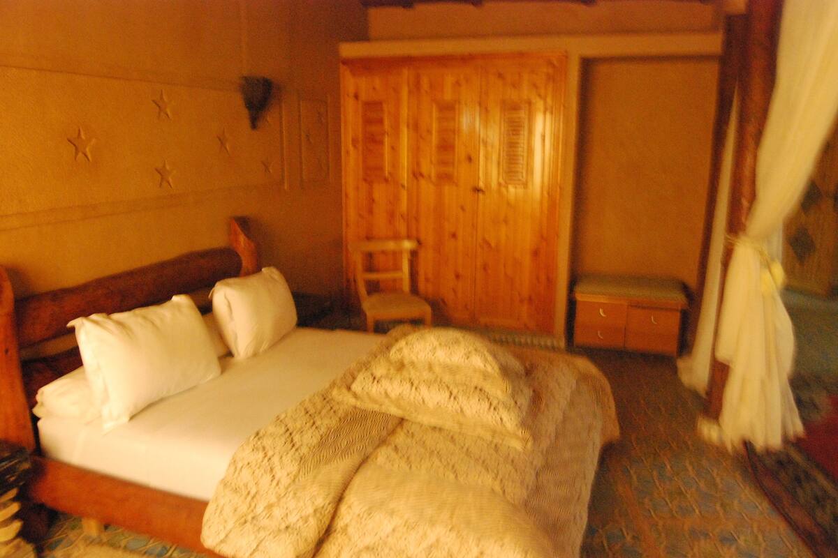 Um quarto aconchegante com uma cama de madeira, um pequeno armário de madeira e uma parede com padrão de estrelas.