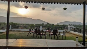 A covered outdoor seating area with tables and chairs, overlooking a mountainous landscape. - The Udaisagar Retreat - Udaipur (Udaipur)