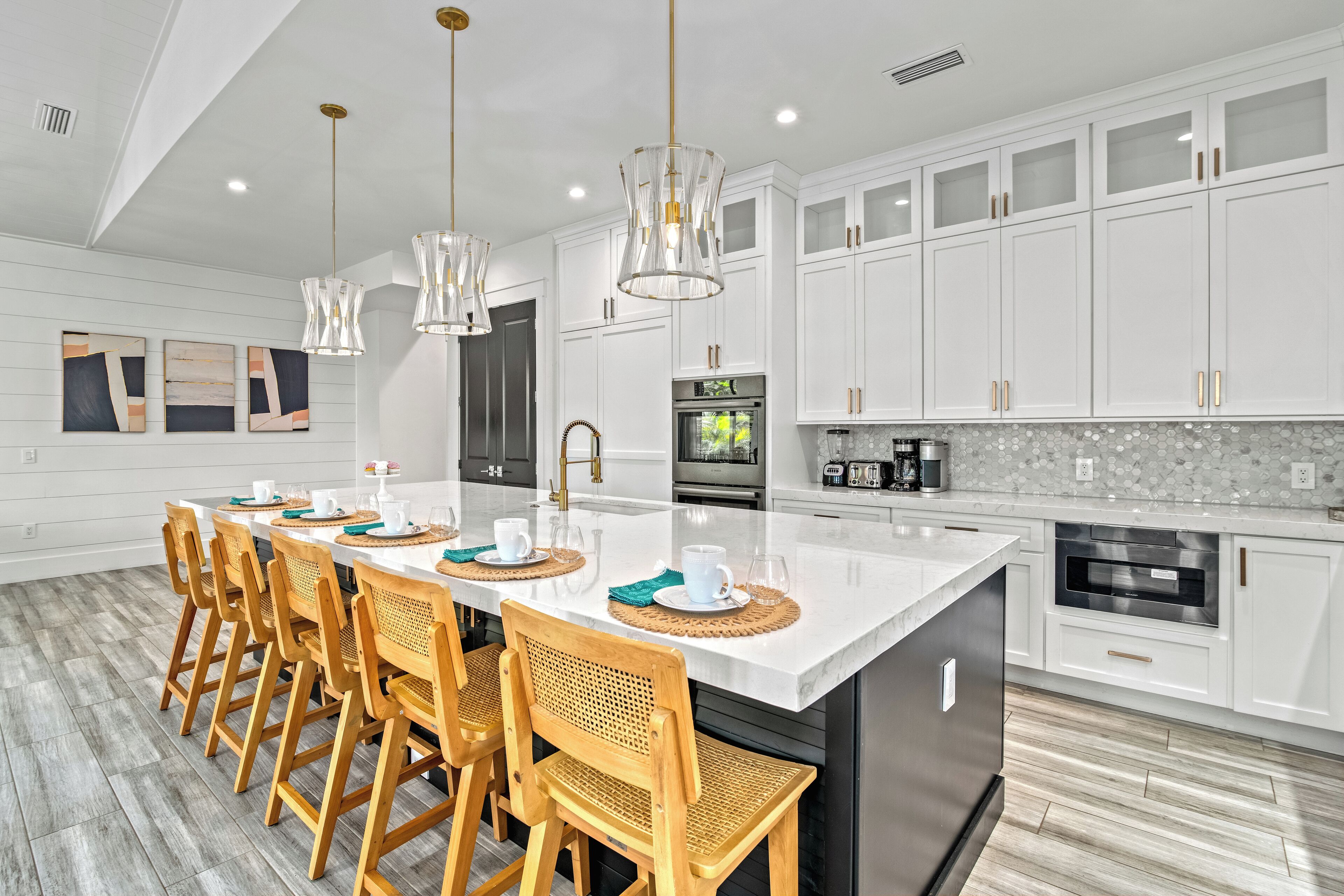 A modern kitchen with white cabinetry, a large island, and a dining area with wooden chairs.