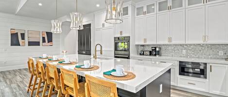 A modern kitchen with white cabinetry, a large island, and a dining area with wooden chairs.