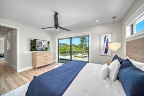 Ein modernes Schlafzimmer mit einem großen Bett, einem Deckenventilator, einem Fernseher auf einer Kommode und Blick ins Freie.