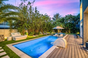 A swimming pool with lounge chairs and a deck, surrounded by lush greenery and a wooden deck. - Sunset Reflections | LUXURY Home, Private Pool, Spa, Rooftop, Game Room, and MORE! (Anna Maria)