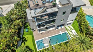A multi-story modern building with a rooftop deck, a swimming pool, and lush greenery. - Sunset Reflections | LUXURY Home, Private Pool, Spa, Rooftop, Game Room, and MORE! (Anna Maria)