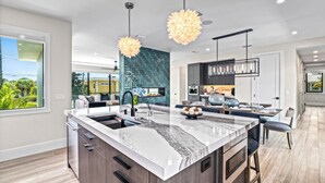 A modern kitchen with a large island, pendant lights, and a view of the outdoors. - Sunset Reflections | LUXURY Home, Private Pool, Spa, Rooftop, Game Room, and MORE! (Anna Maria)