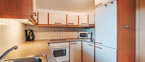 Una cocina compacta con gabinetes blancos, un microondas, una estufa y un lavamanos.