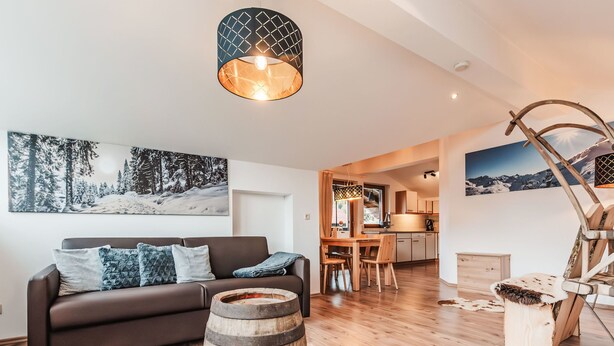 Ein modernes Wohnzimmer mit Holzboden, einem dunkelbraunen Sofa, einem Holzbottich und einem großen Gemälde einer verschneiten Landschaft.