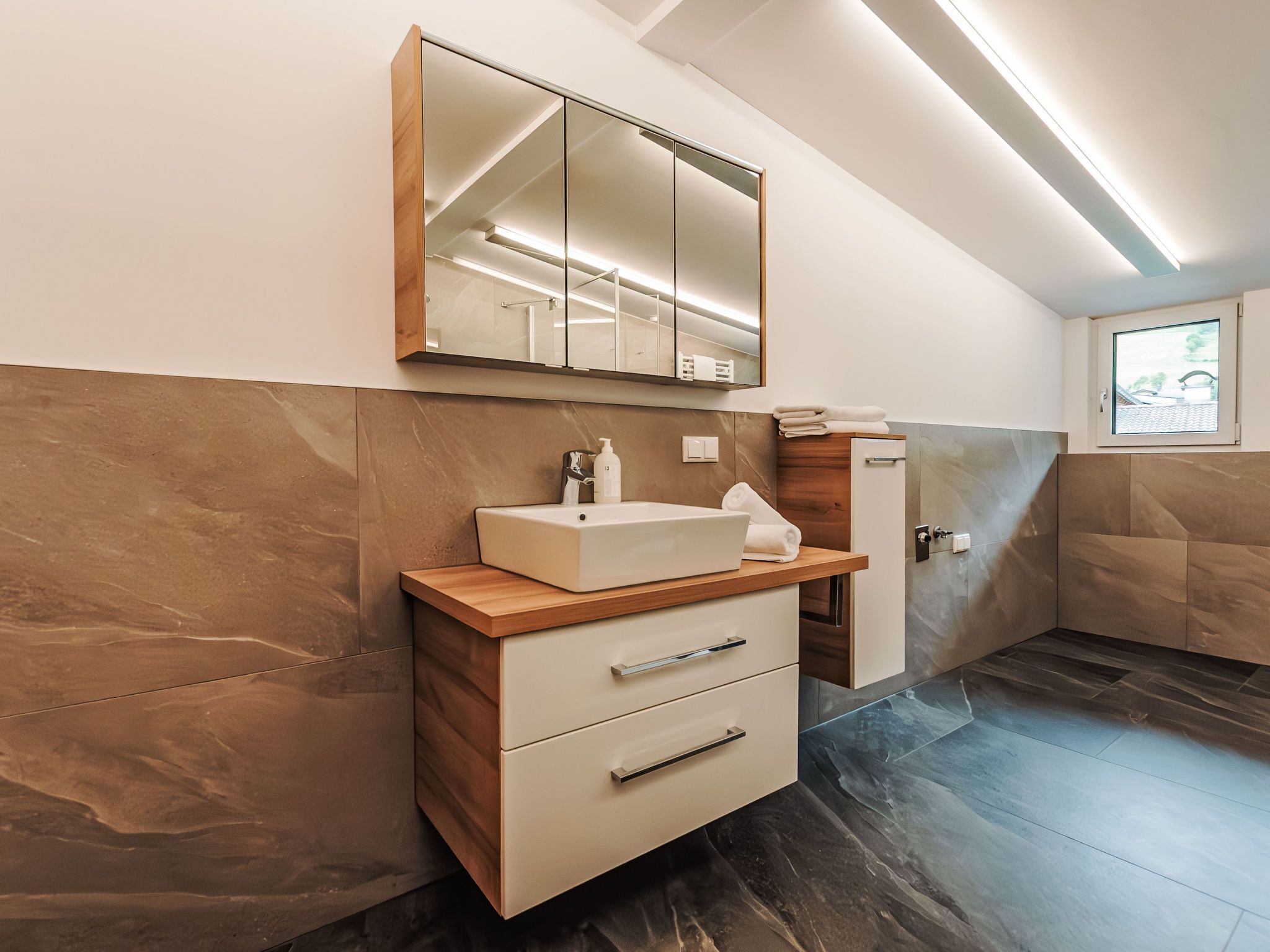 A modern bathroom with a large mirror, a sink, and a cabinet.