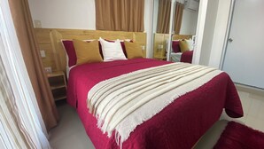 A bedroom with a wooden bed frame, red and white bedding, a beige throw blanket, and a large mirror above the bed.