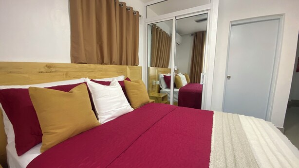 A hotel room with a wooden headboard, a large bed with red and white bedding, a mirror, and a sliding door leading to a bathroom.