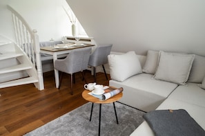 A modern living room with a wooden staircase, grey chairs, a white sofa, and a small round table with a teapot and cups. - Friesenstübchen - Modernes App. für bis zu 3 Pers. in Stadt- und Strandnähe, Inkl. Parkplatz (Westerland)