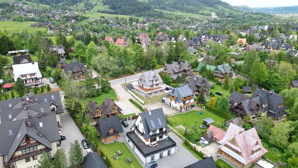 Un barrio residencial con casas de techos pronunciados y exteriores de madera, rodeado de abundante vegetación y un paisaje montañoso.