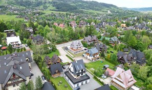 A residential area with houses featuring steep roofs and wooden exteriors, surrounded by lush greenery and a hilly backdrop.