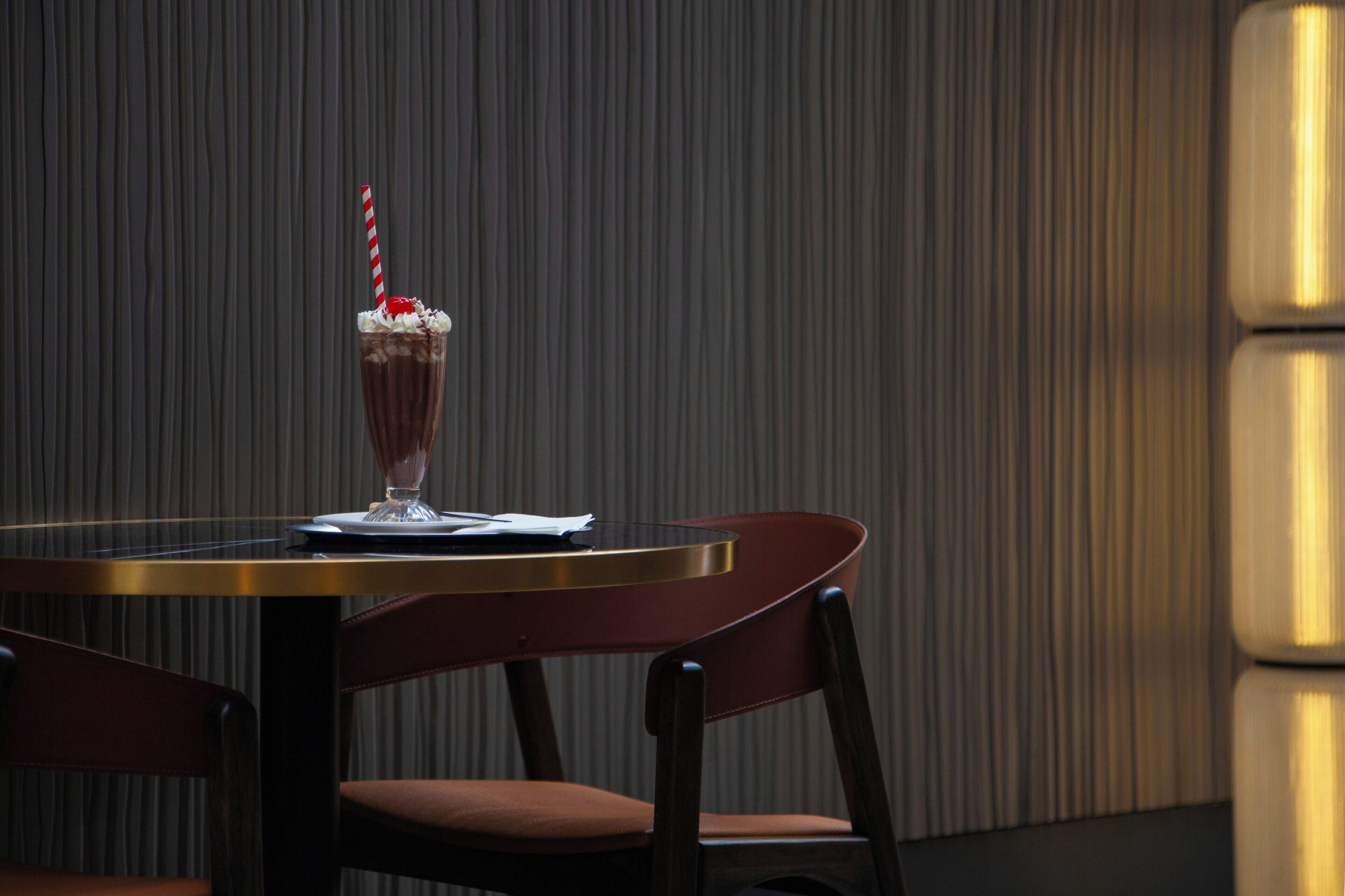 Una mesa de comedor con un postre, una silla y una pajita a rayas.