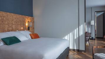 Une chambre d’hôtel moderne avec un grand lit, une tête de lit en bois, une table de chevet et une vue sur le couloir.