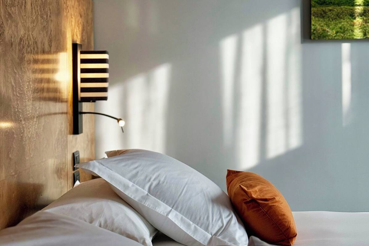 Un dormitorio con cama, almohadas, una lámpara de pared e imagen enmarcadas.