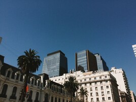 A cityscape with modern and historic buildings, including a prominent glass skyscraper and a classical building with columns.