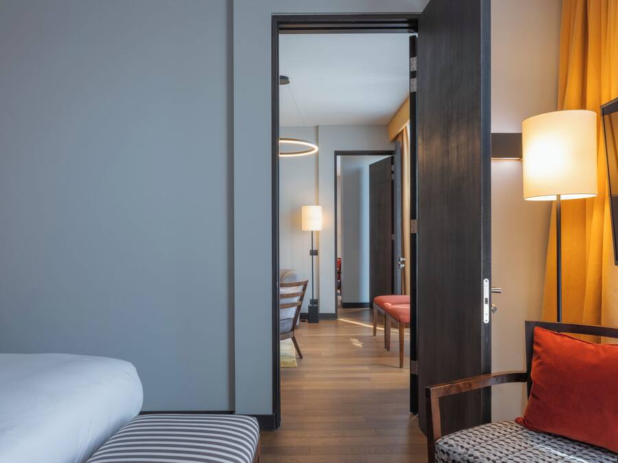 A hotel room with a bed, a chair, a desk, and a lamp.