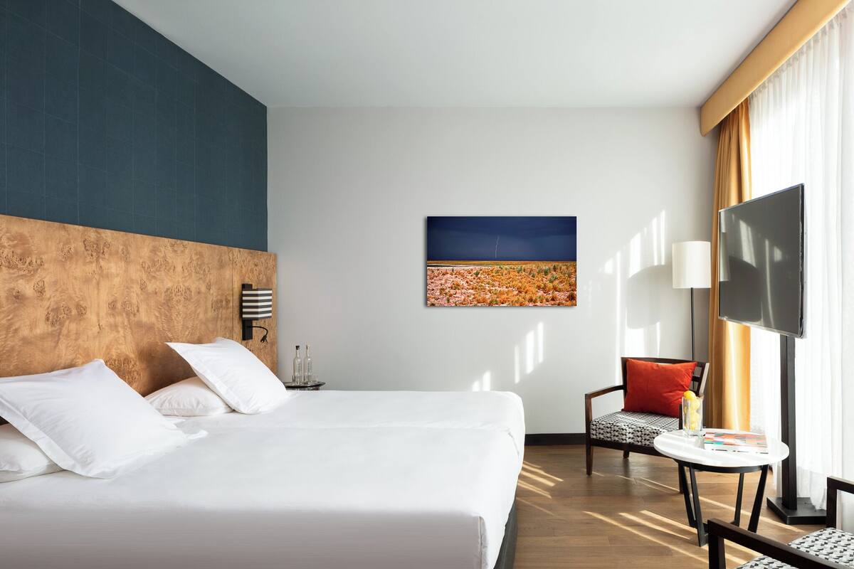 Habitación de hotel con una cama grande, un televisor de pantalla plana, una mesita pequeña y una silla.
