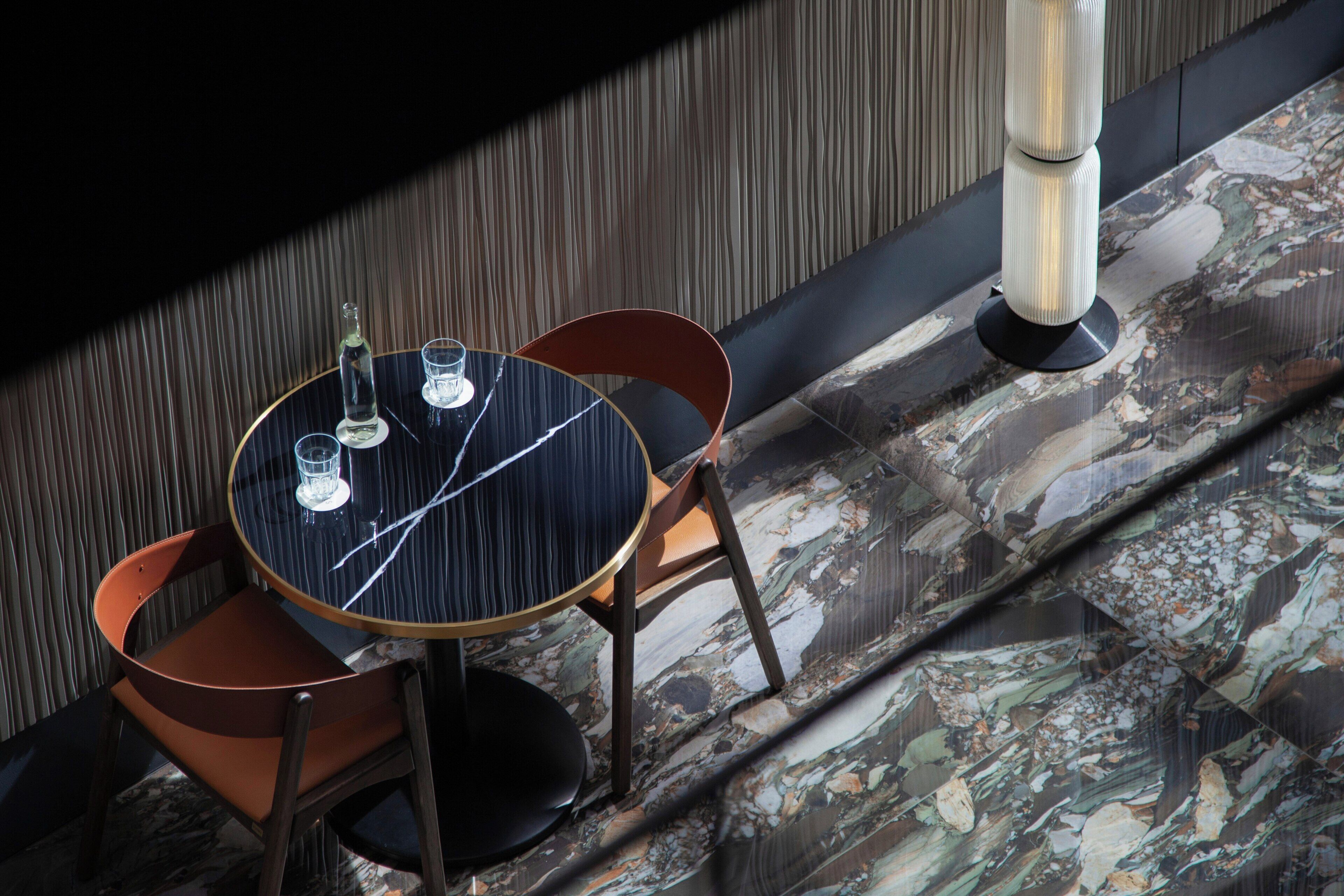 A round table with chairs, a bottle, and glasses on a patterned floor.