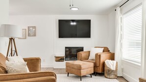 Een woonkamer met een open haard, een grote flatscreen televisie en een raam met zonwering.