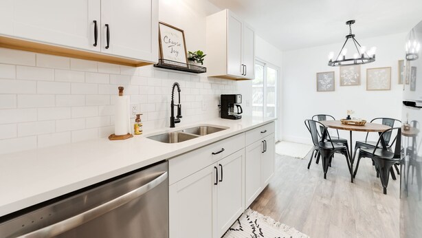 Een moderne keuken met witte kasten, roestvrijstalen apparatuur en een eethoek met zwarte stoelen en een houten tafel.