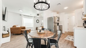 Een moderne keuken met witte kastjes, een roestvrijstalen koelkast en een eethoek met een ronde houten tafel en zwarte stoelen.