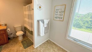 Ein Badezimmer mit Toilette, Duschvorhang, Handtuchhalter und einem Fenster mit Jalousien.