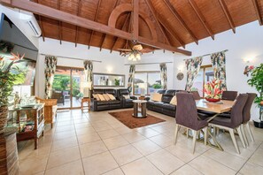 A spacious living room with a high ceiling, a wooden dining table with chairs, a sofa set, and a cat tree.