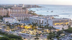 A hotel with multiple buildings, a parking lot, and a view of the ocean with boats.
