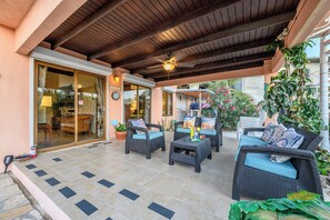 An outdoor patio with wicker furniture, a ceiling fan, and potted plants.