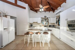 A modern kitchen with white cabinets, a central island with stools, a ceiling fan, and built-in appliances.