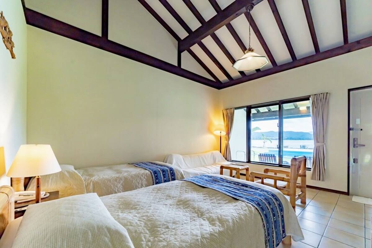 Een hotelkamer met twee bedden, een raam met uitzicht, een bureau met lamp en een stoel.