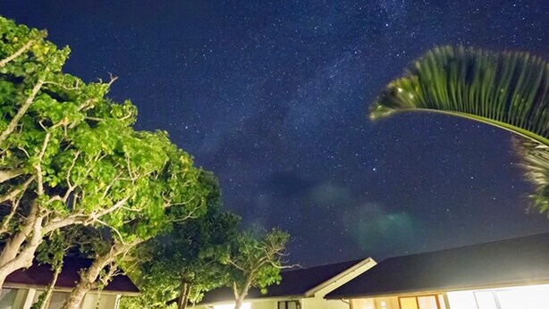 A nighttime view of a residential property with a swimming pool, trees, and a house with large windows and a sloped roof. - VILLA  UNARIZAKI (Taketomi)