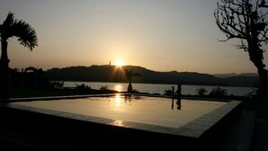 A swimming pool with a sunset view, surrounded by trees and a distant hill. - VILLA  UNARIZAKI (Taketomi)