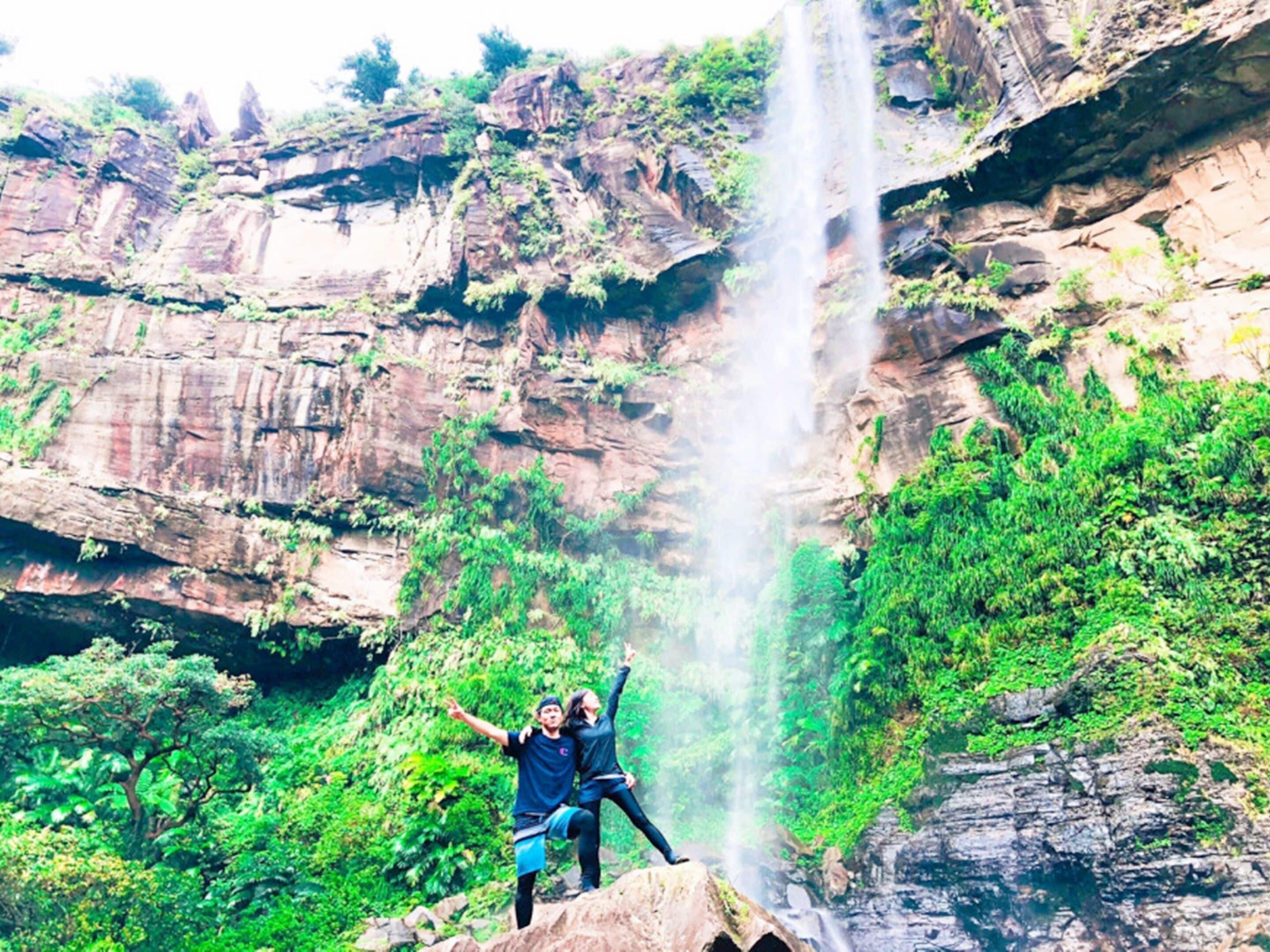 Een waterval met twee personen die poseren op een rotsplateau.