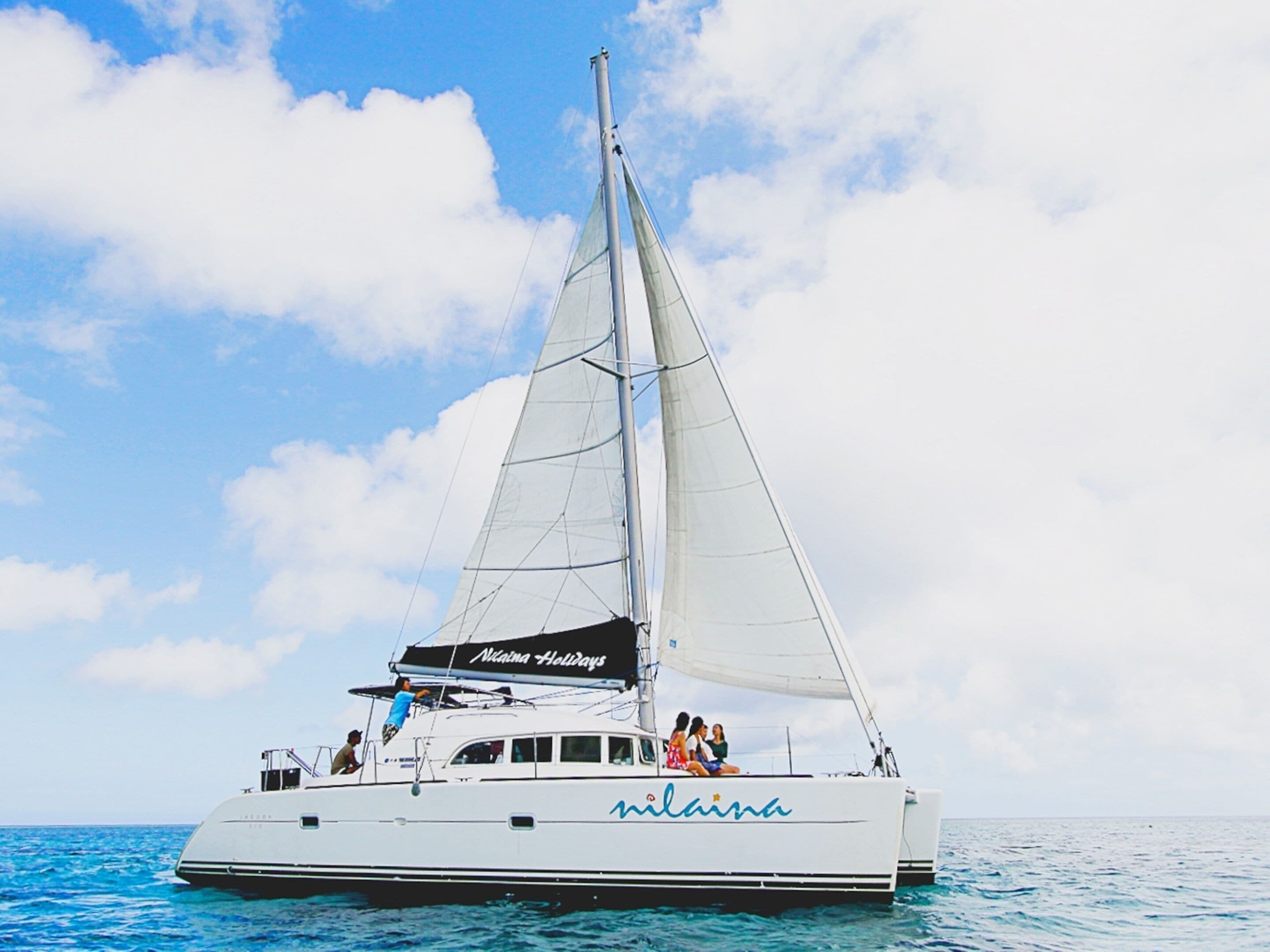 A white sailboat with the name "Nina" on its side, sailing on clear blue water.