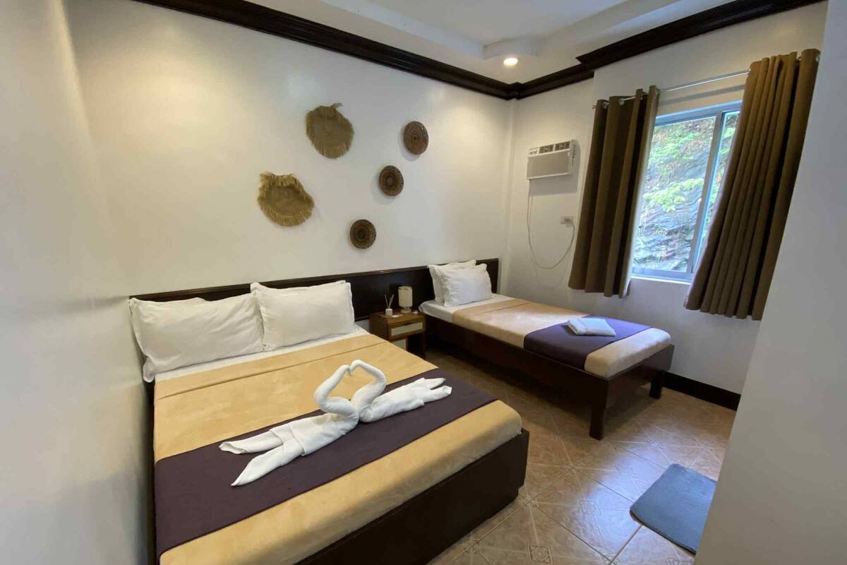 A hotel room with two beds, a window with curtains, a wall-mounted air conditioner, and decorative wall art.